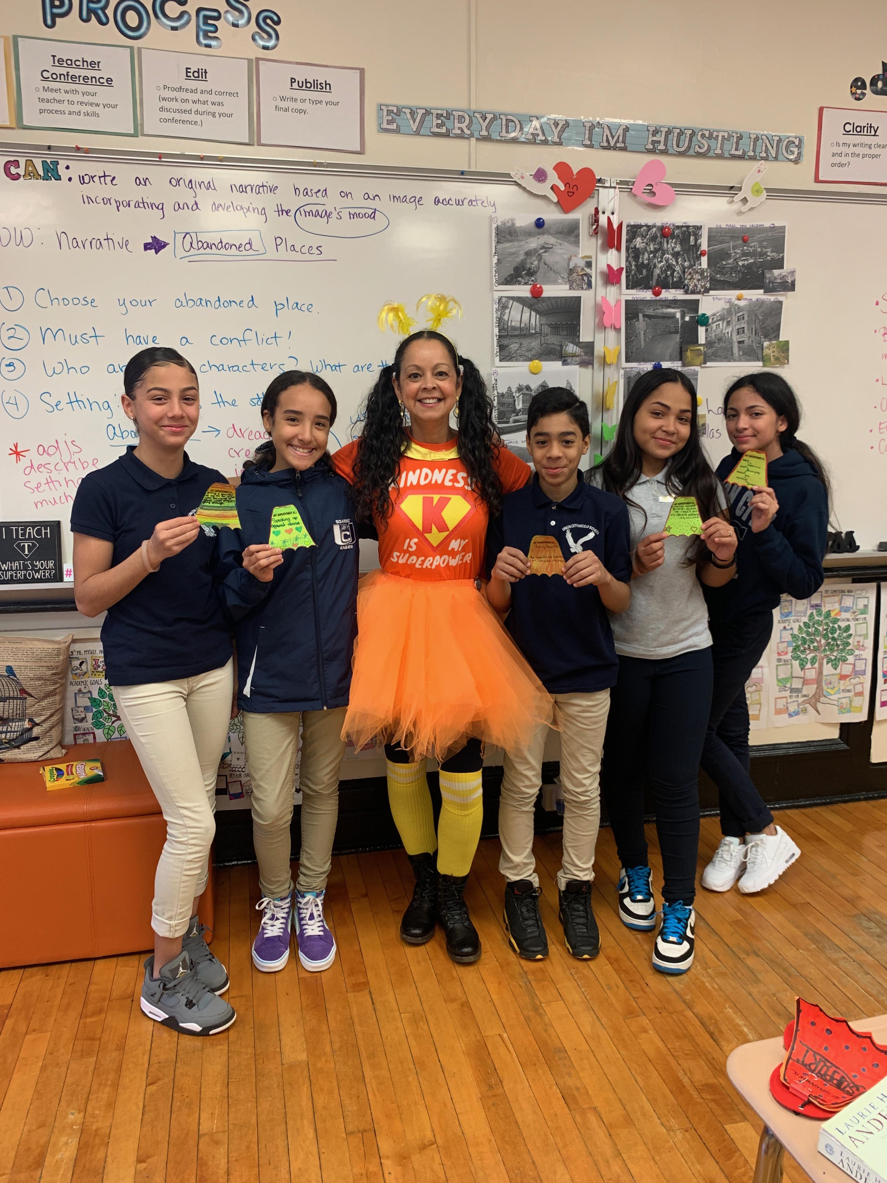 Ms. Garcia dressed as Kindness Superwoman with four girls holding their paper capes and one boy side by side