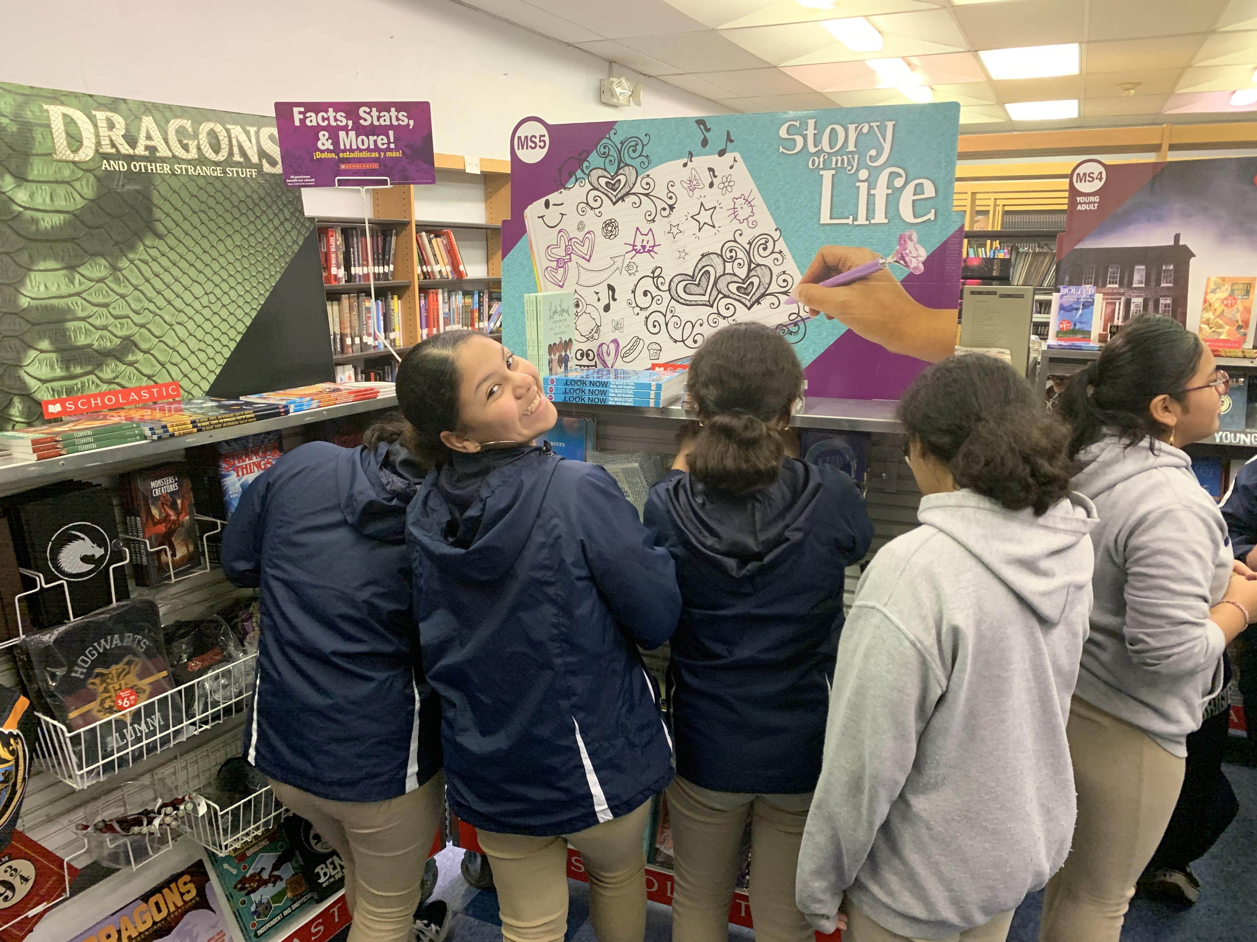 students looking at the books while a girl looks back and smiles