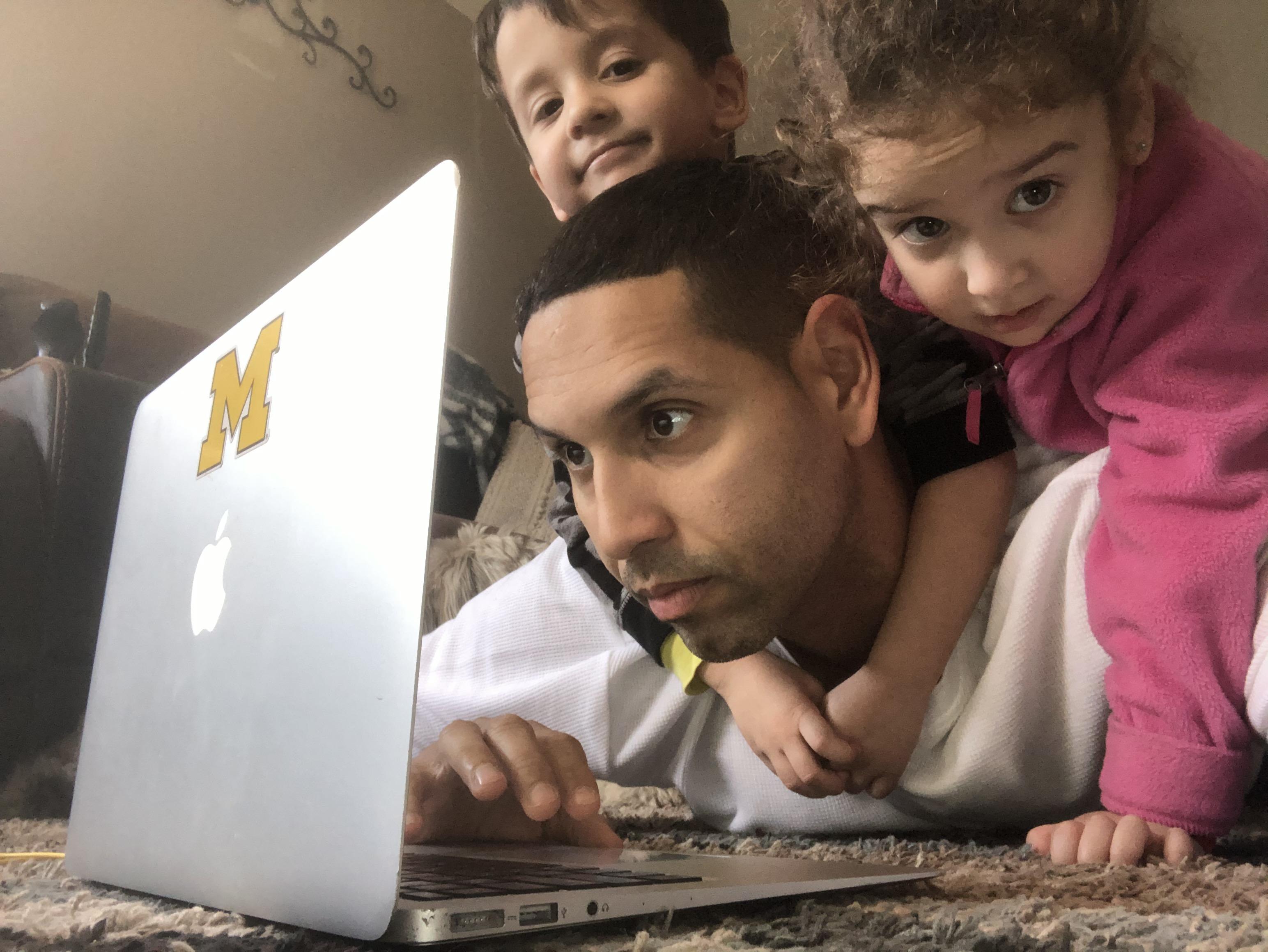 teacher working on laptop with his two children on him